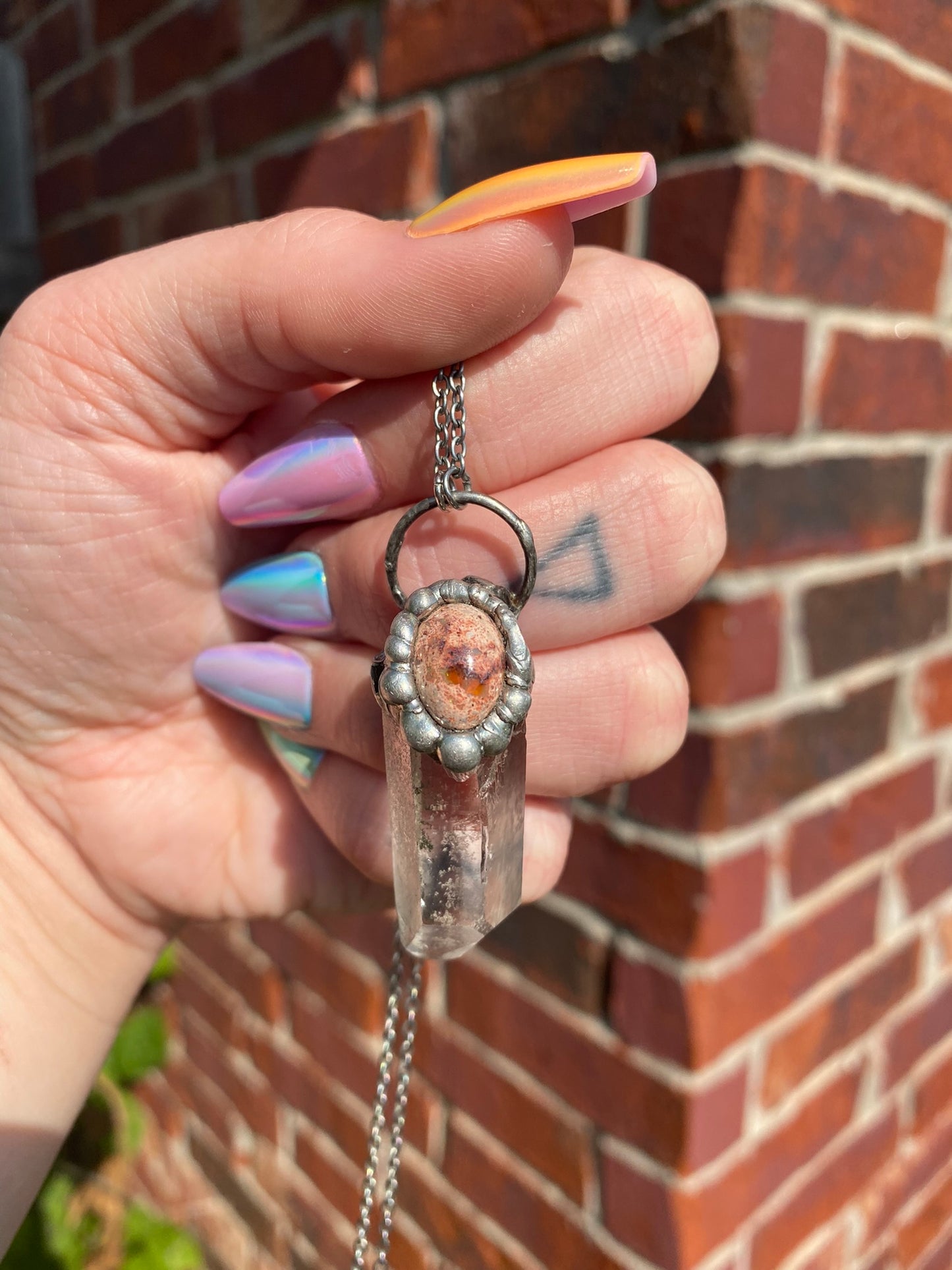 hand holding quartz + mexican fire opal pendant in front of brick wall