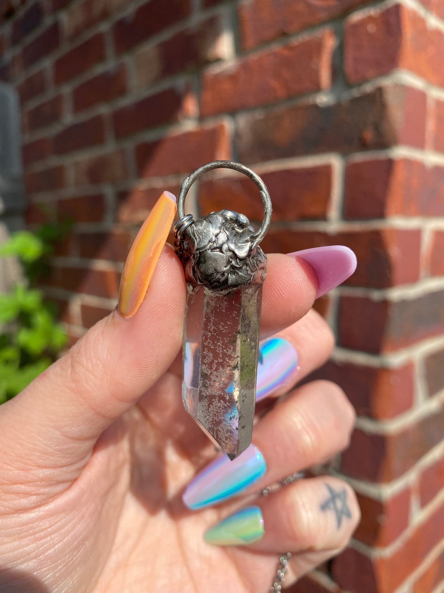 hand holding quartz + mexican fire opal pendant in front of brick wall