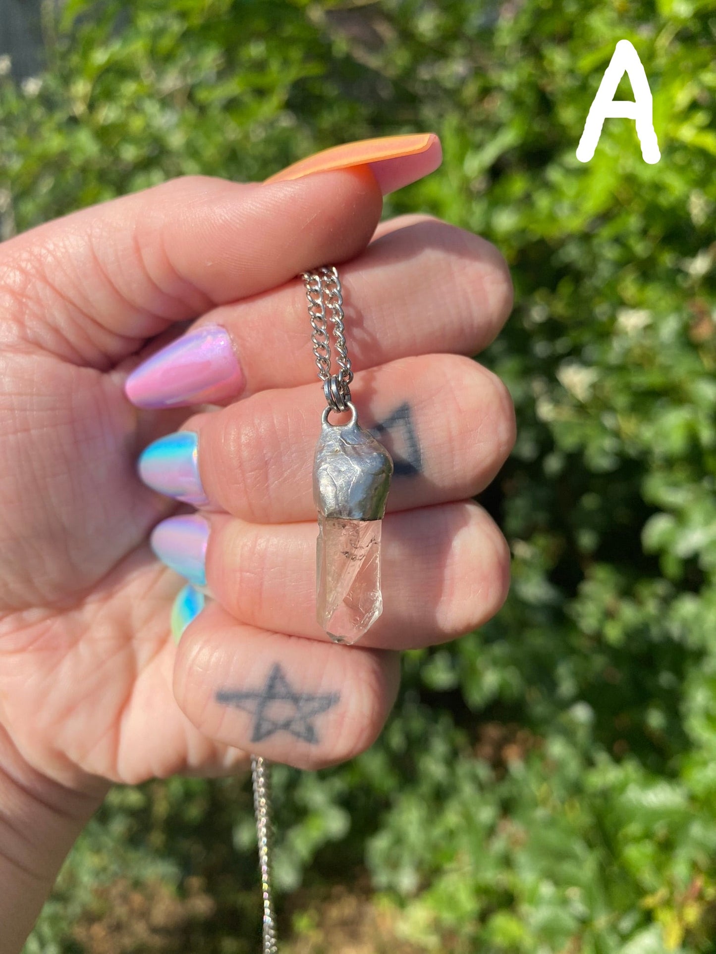 hand holding simple quartz pendant style "a" in front of a rose bush