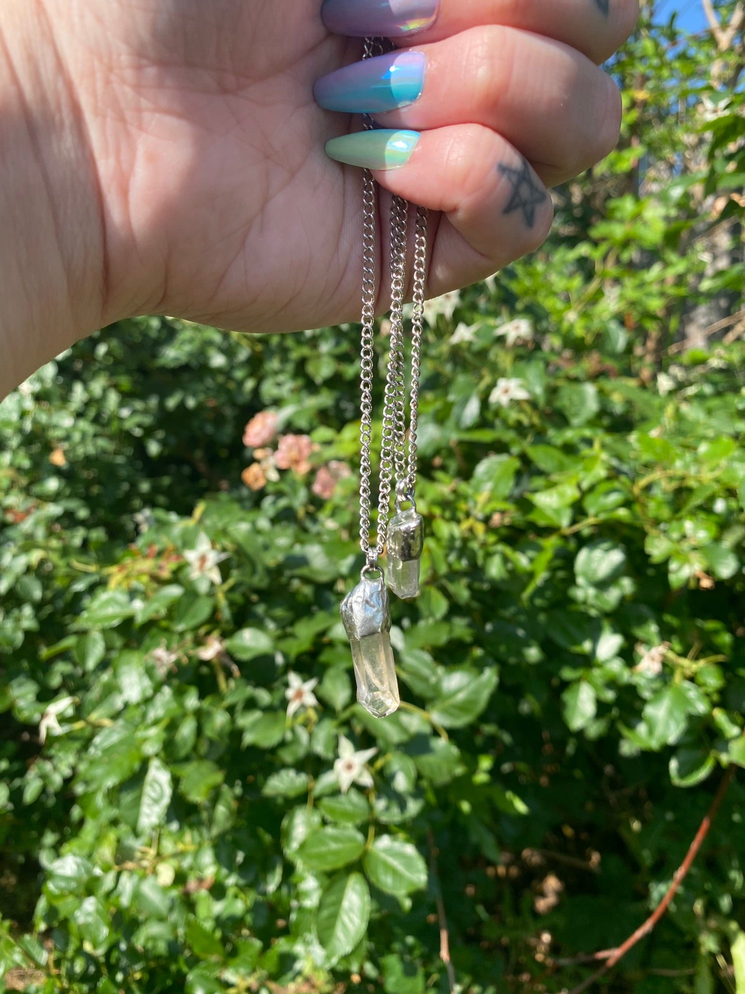 hand holding two simple quartz pendants in front of a rose bush