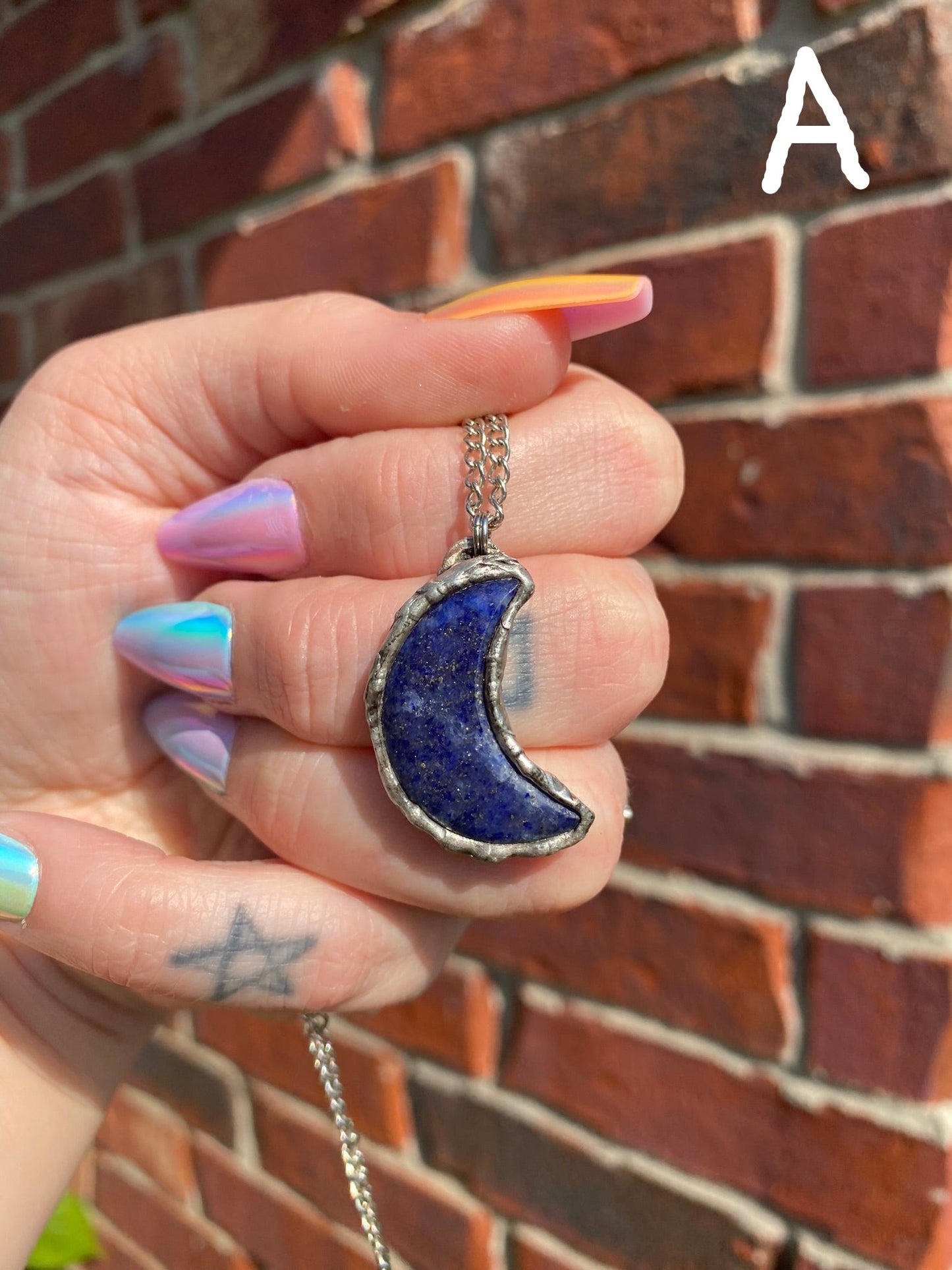 hand holding lapis lazuli crescent moon pendant in front of a brick wall