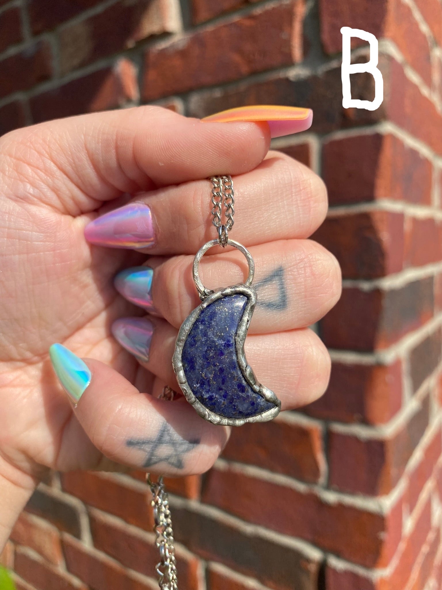 hand holding lapis lazuli crescent moon pendant in front of a brick wall