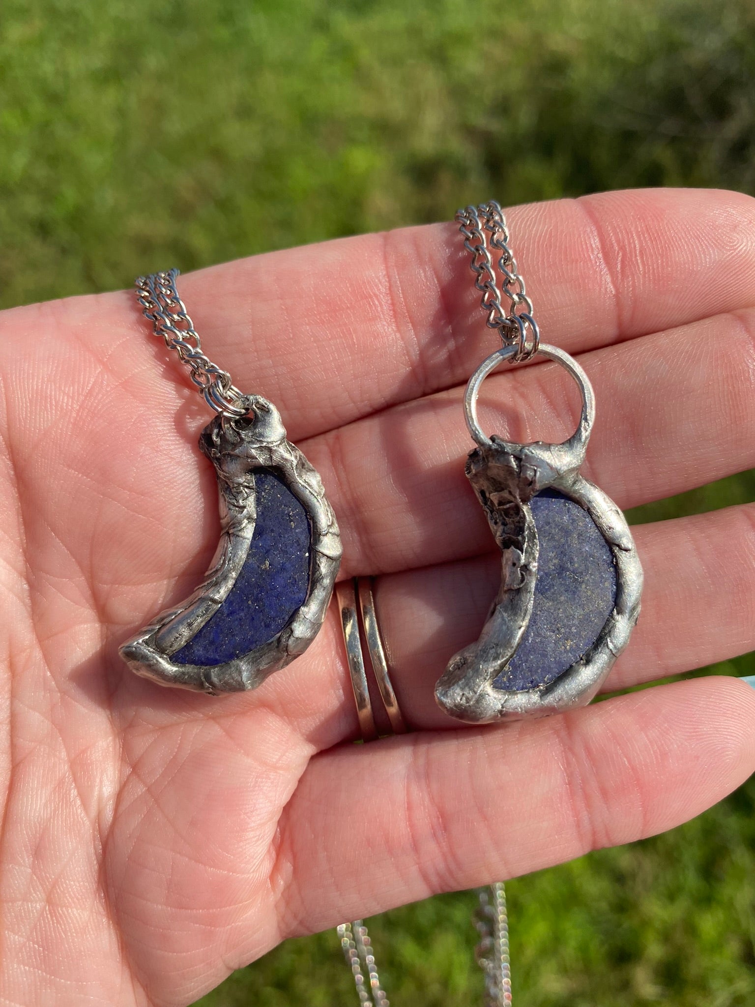 hand holding two lapis lazuli crescent moon pendants in front of grass