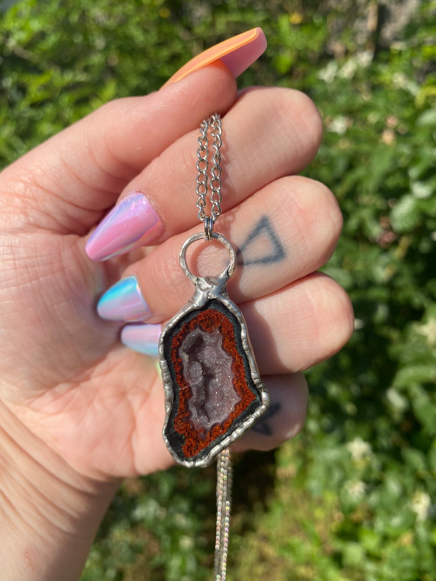 hand holding agate pendant in front of a rose bush