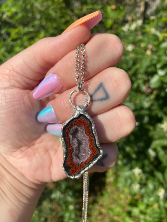 hand holding agate pendant in front of a rose bush