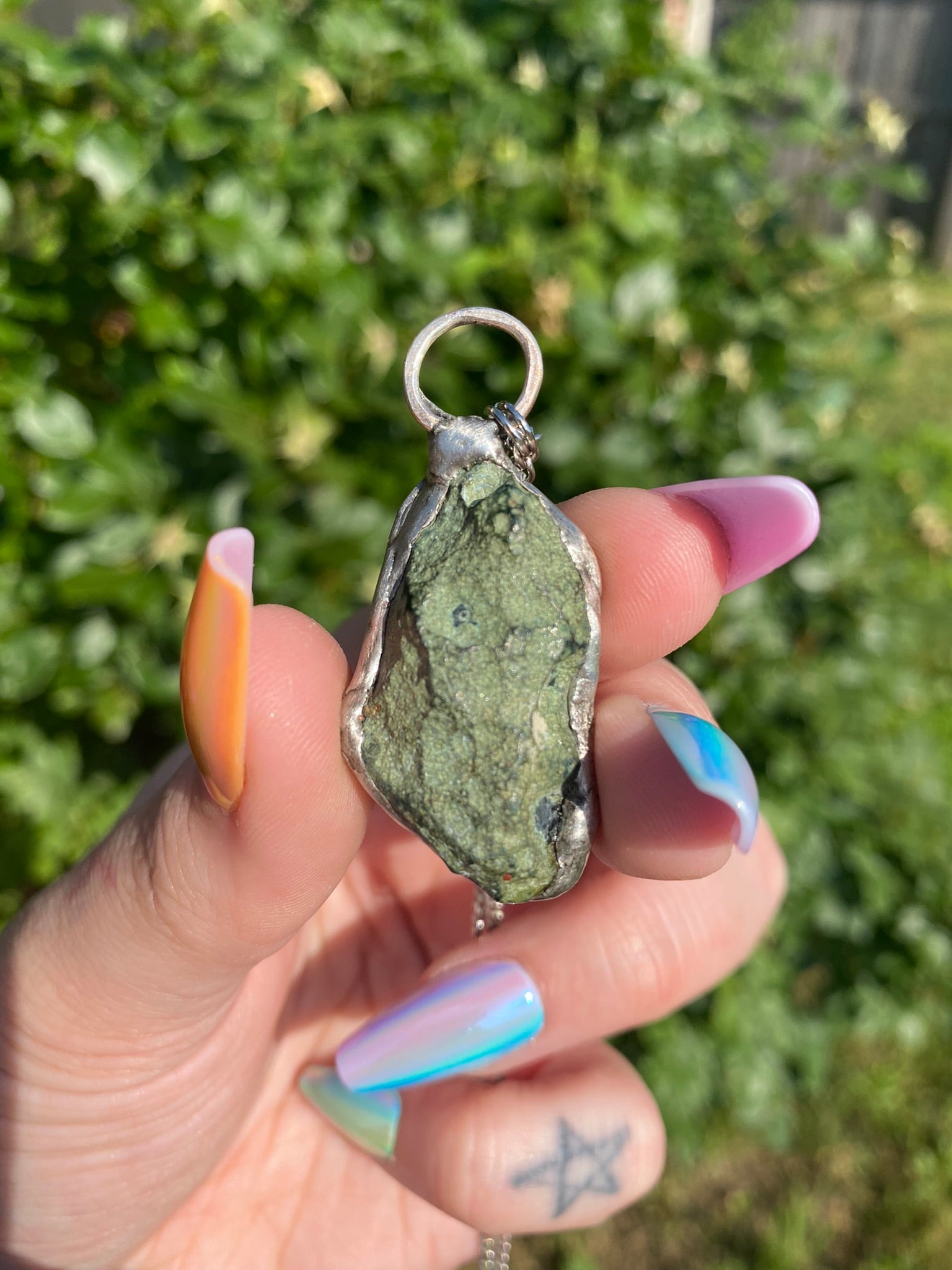 hand holding agate pendant in front of a rose bush