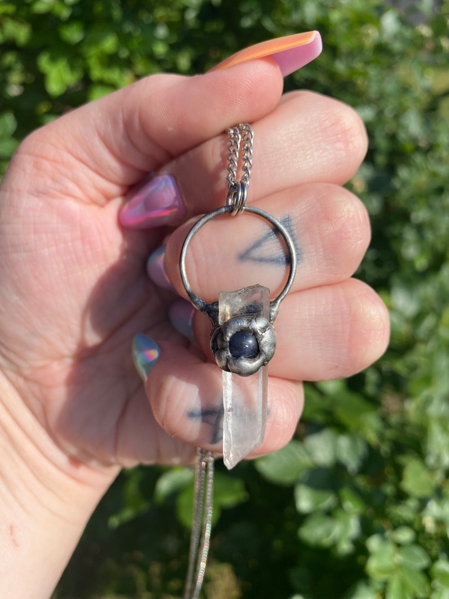 hand holding a quartz + sodalite pendant in front of a rose bush