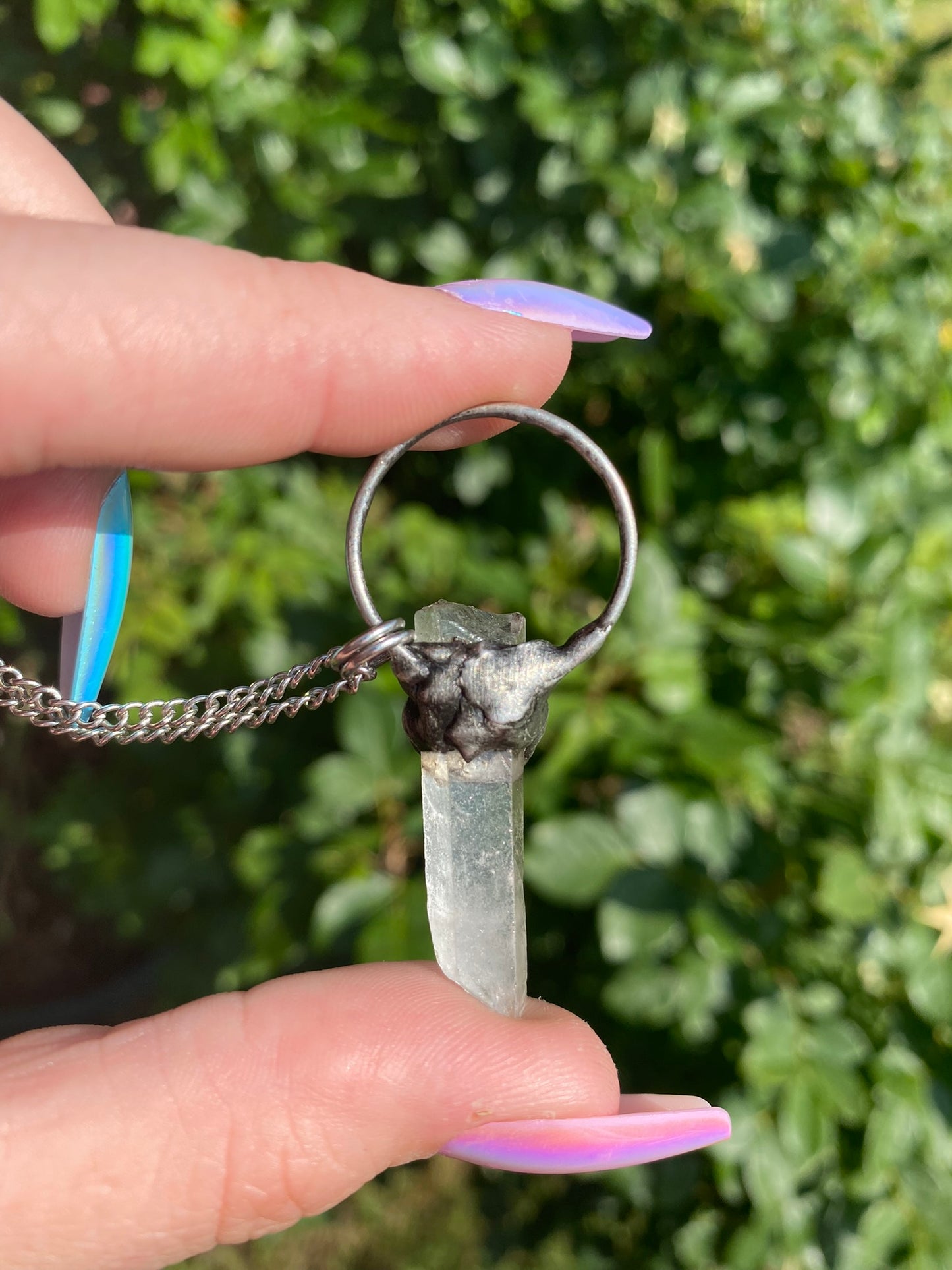 hand holding a quartz + sodalite pendant in front of a rose bush