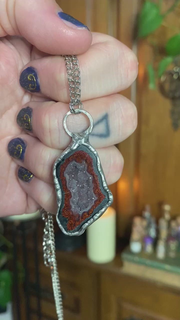 short video of hand holding agate pendant in front of a witchy background