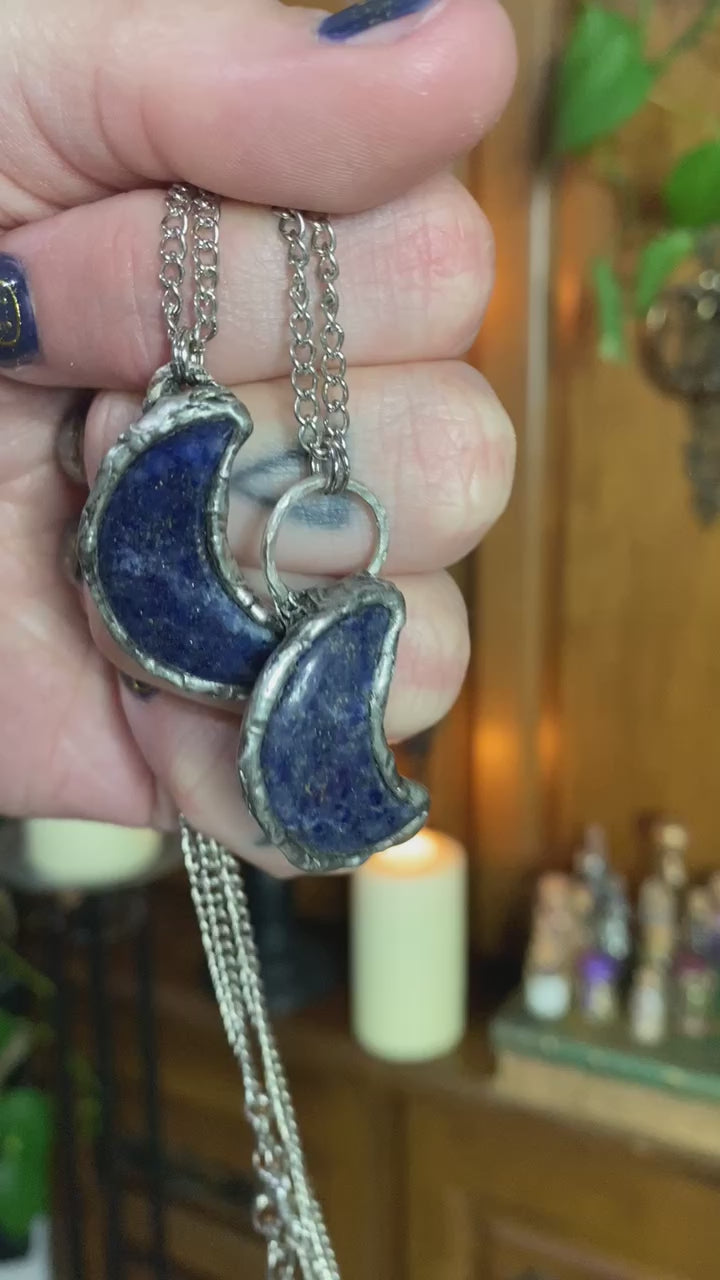 short video of hand holding two lapis lazuli crescent moon pendants in front of witchy background