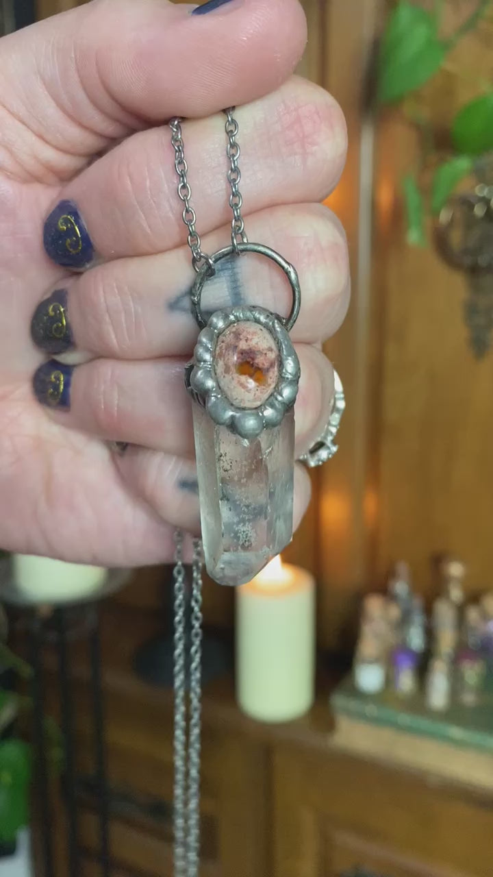 short video of hand holding mexican fire opan + quartz pendant in front of witchy background